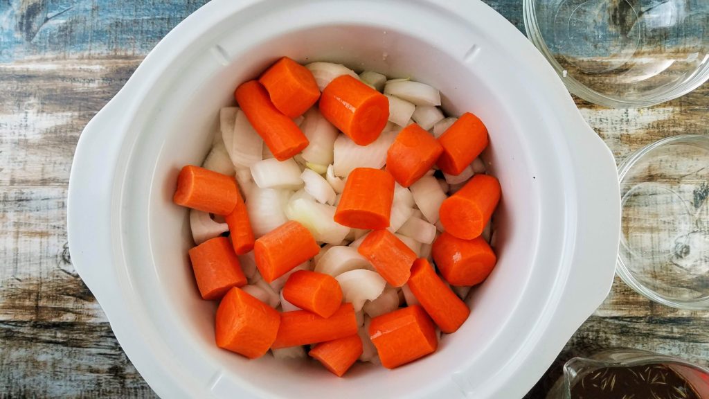 Slow cooker filled with diced carrots and onions