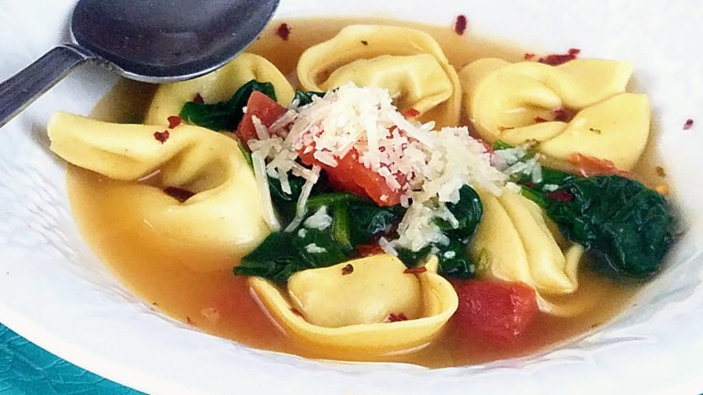 bowl of tortellini with spinach and tomatoes in broth