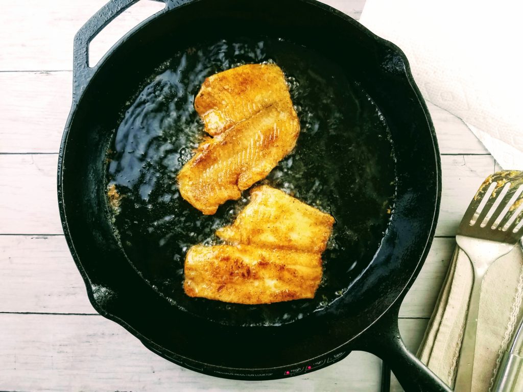 Flounder fillets frying in a cast iron pan